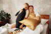boy and girl sit on a bed hugging pillows with silk pillowcases