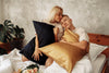 boy and girl sit on a bed hugging pillows with silk pillowcases