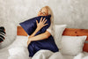 woman is hugging her pillow with blue silk pillowcase and looking happy